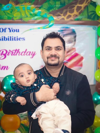 A father holds his baby in front of a fun, colorful birthday banner.