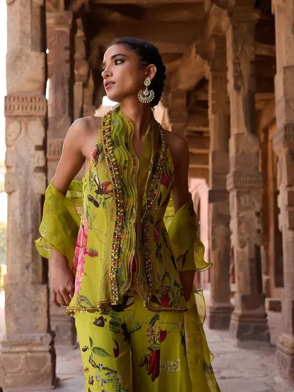A model stands gracefully in a lime green floral peplum top and matching pants. The ruffled dupatta adds a touch of romantic flair to this fresh, modern look.