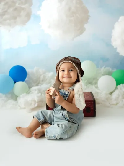 An adorable little aviator sits amongst fluffy clouds for his themed baby photoshoot. His happy smile is absolutely infectious.