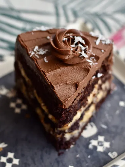 A decadent slice of our German Chocolate Cake. You can see the rich layers of dark chocolate cake, a fudgy coconut and walnut filling, and a smooth 54% chocolate ganache. We believe what's inside matters most.