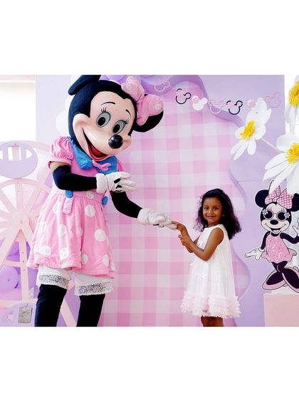 The birthday girl shares a sweet moment with the Minnie Mouse mascot. The backdrop features a pink and white gingham pattern and daisy props, matching the theme perfectly.