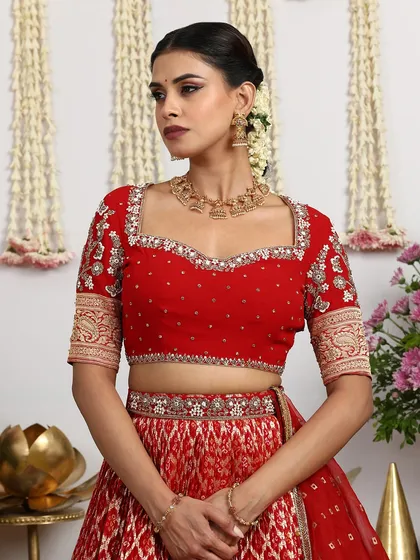 A close-up of the red bridal blouse, showcasing the detailed embroidery around the sweetheart neckline and on the brocade sleeves. Every detail is crafted to perfection.