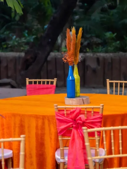 A simple yet effective centerpiece using painted bottles and dried flowers, adding a pop of color to the bright orange tablecloth.