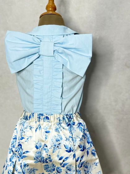 A sweet and stylish shorts set. The blue floral shorts are paired with a light blue shirt featuring a large, elegant bow on the back.