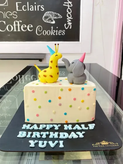 A cute and simple half-birthday cake. The design features colorful polka dots and is topped with a tiny fondant giraffe and elephant wearing party hats.