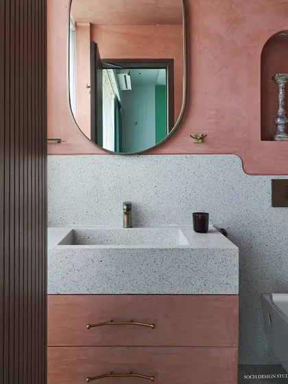 A detail of the bathroom vanity, showing the terrazzo countertop and sink, paired with brass fixtures and a custom mirror. The design focuses on natural materials and clean, curved lines.