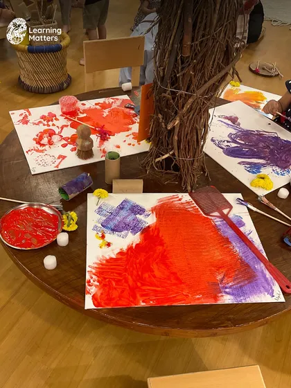 This table is a canvas for collaborative art. Using various tools like rollers and fly swatters, children explore different ways to apply paint, discovering new patterns and textures together. The focus is on shared creation, not a single outcome.