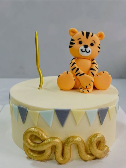 A sweet and simple first birthday cake featuring a cute, handcrafted tiger topper. The soft colors and clean design are perfect for celebrating your little one's big milestone.