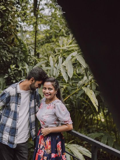 A candid and romantic shot of a couple from their pre-wedding shoot, framed by lush green leaves.