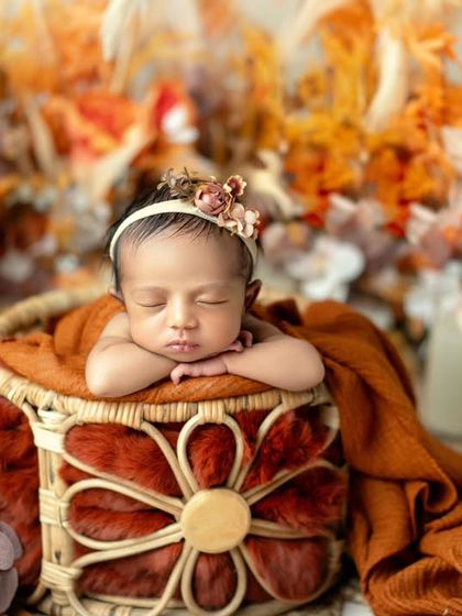 Sunshine and sleepy sighs. This newborn is peacefully posed in a basket with warm, autumnal colors, creating a cozy and inviting portrait.