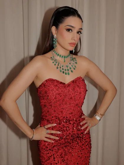 A powerful pose showing off the vibrant red gown. The makeup enhances her features with a defined eye and glowing skin.
