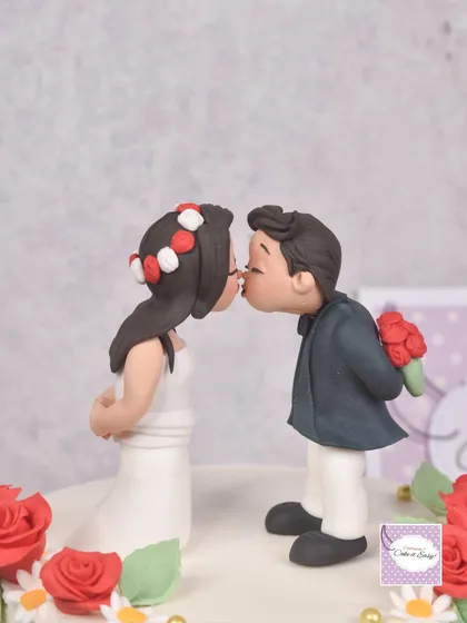 A sweet and simple anniversary cake topper. This kissing couple was hand-sculpted from fondant, complete with a tiny bouquet of red roses, perfect for celebrating a first anniversary.