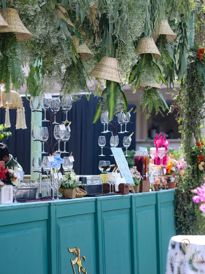 A closer look at the botanical bar, showing the hanging glass racks and the lush greenery canopy with woven lampshades.
