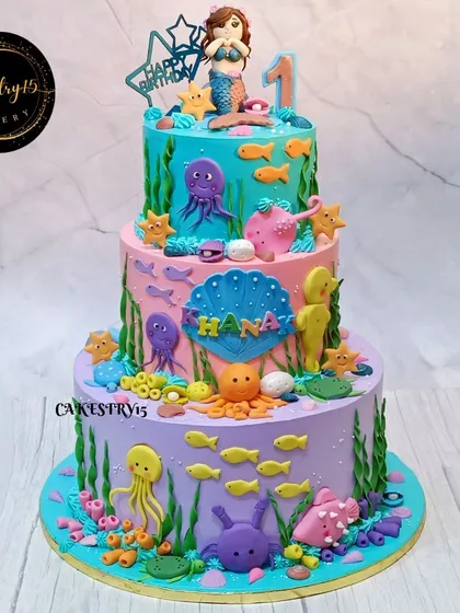 An impressive 8kg, three-tier mermaid-themed cake. This underwater masterpiece is decorated with a fondant mermaid, sea creatures, and colorful coral reefs for a spectacular first birthday.