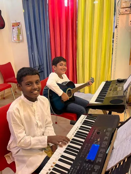 Our classes often have students learning different instruments side by side. Here, you can see one student practicing on the keyboard while another is on the acoustic guitar, creating a dynamic and collaborative learning space.