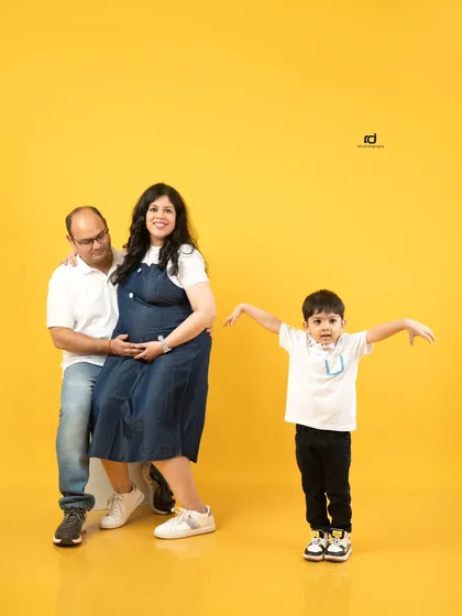 A fun and candid family moment against a bright yellow backdrop. The older brother's playful pose brings so much energy and joy to this family maternity photo.