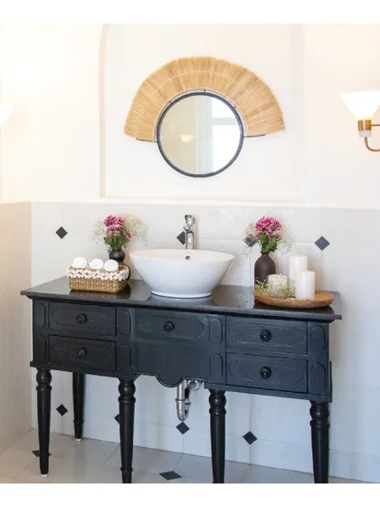 The son's bathroom in the Goa holiday home is a playful combination of black and white tiles. We paired this classic pattern with a walnut vanity counter and a quirky cane mirror to add a touch of tropical charm.