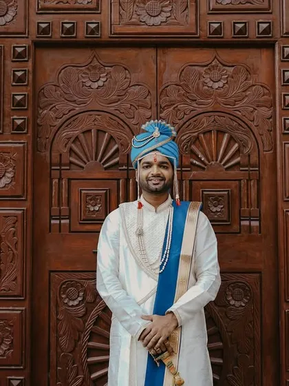 A confident and happy portrait of the groom in his traditional wedding attire, standing before an ornate wooden door.