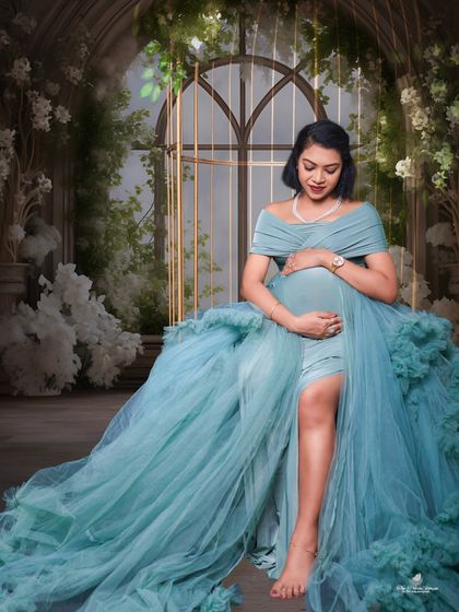 A quiet, contemplative moment. The mom-to-be looks down at her bump, seated in a beautifully styled set that combines glamour with a touch of nature.