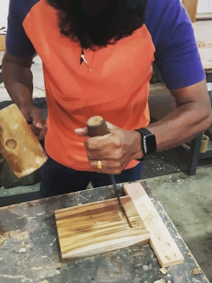 A student uses a mallet and chisel to carefully carve out a mortise joint. This demonstrates the precision and skill involved in traditional joinery techniques.