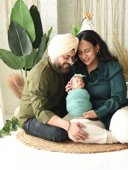 A beautiful family portrait with their newborn baby, swaddled in a complementary green wrap. This image showcases the full boho-chic setup, complete with pampas grass, lanterns, and macrame details.