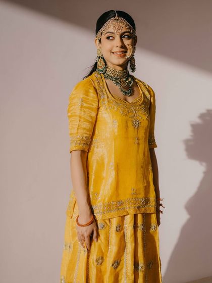 A full-length portrait of the bride in her traditional Rajasthani yellow poshak. The look is a beautiful blend of heritage and timeless elegance.