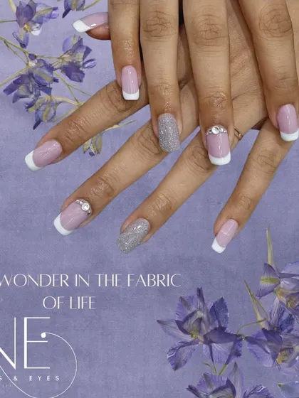 A classic French manicure with a touch of sparkle. This set features clean white tips on a square-shaped nail, with two accent nails in silver glitter and rhinestone details at the cuticle.