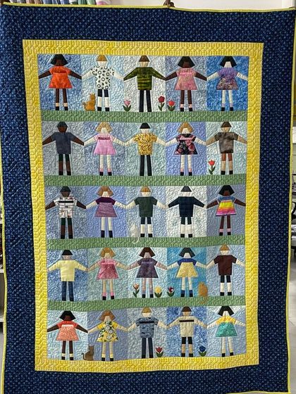 A heartwarming "Paper Doll" quilt, featuring rows of children holding hands, each with unique clothing made from different fabrics.