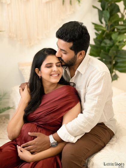 An intimate and loving couple's portrait taken in a soft, naturally lit room. The partner gently kisses his smiling partner's forehead as they both cradle the baby bump.