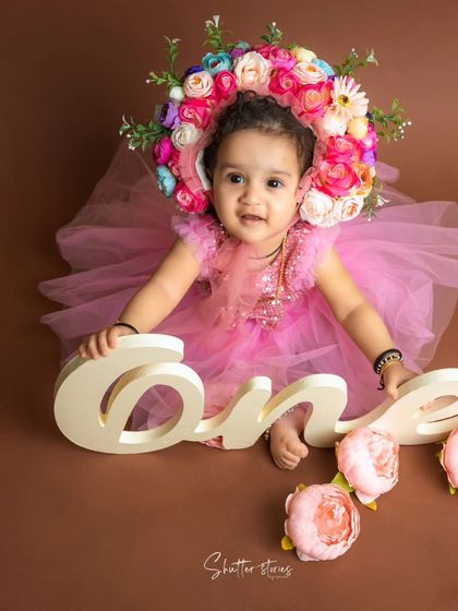 This little girl in a pink dress and a stunning floral bonnet is celebrating her first birthday.