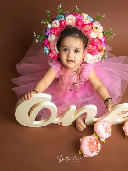 This little girl in a pink dress and a stunning floral bonnet is celebrating her first birthday.