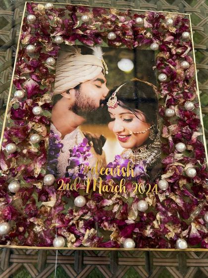 An overhead view of the floral photo frame, highlighting the arrangement of the purple orchid petals and pearls. The gold text with the couple's hashtag and wedding date adds a personalized touch.