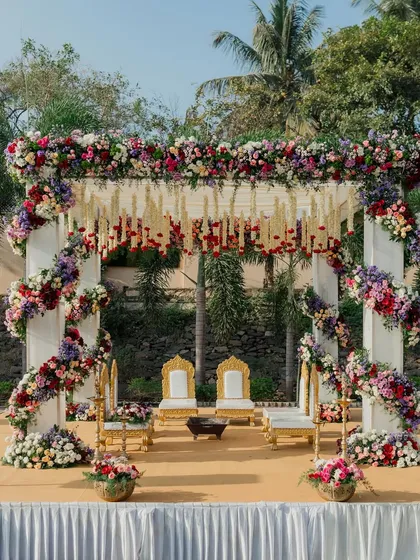 An outdoor wedding mandap that feels both grand and deeply connected to nature. We used a profusion of colorful, fresh flowers to create a vibrant arch, complemented by traditional seating and hanging floral strings, all set against a beautiful natural backdrop.
