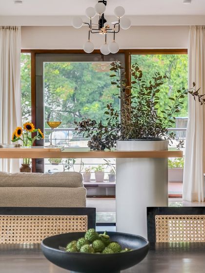 The breakfast unit, with its clean white pillar and wooden top, serves as a connection between the living and dining areas. The view from the dining chairs looks out into the bright, open living space, making the entire home feel connected.