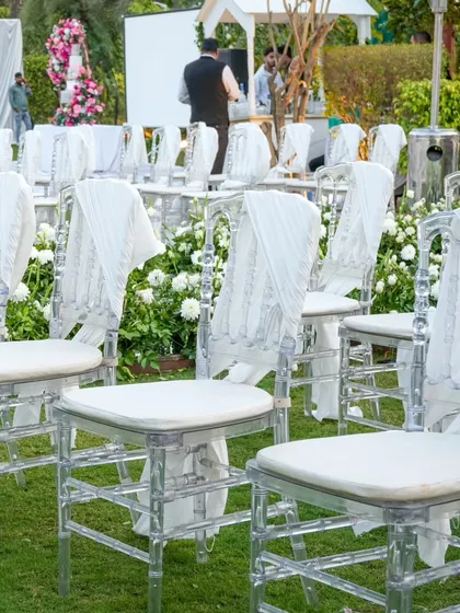 Chic and elegant seating for a sundowner event. Transparent Chiavari chairs are adorned with delicate white drapes, adding a touch of sophistication.
