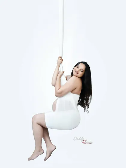 A joyful and carefree pose on the aerial silk swing. The mother-to-be's happy expression makes this a lighthearted and beautiful artistic maternity photo.