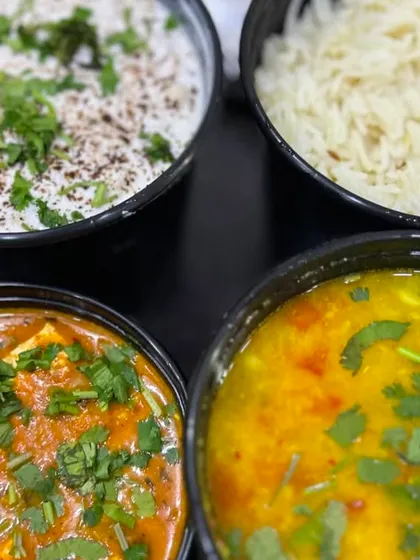 A closer look at the delicious spread of Kadai Paneer, Dal, Rice, and Raita. All dishes are garnished with fresh coriander.