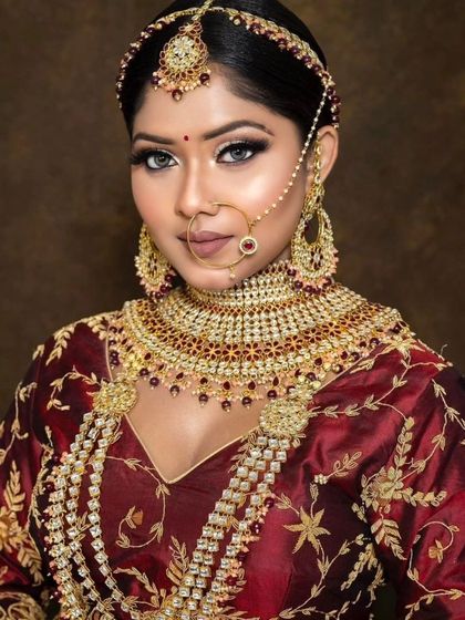 A bride wearing a maroon blouse with a heavy, layered red and gold jewellery set. The look is traditional and perfect for a wedding ceremony.