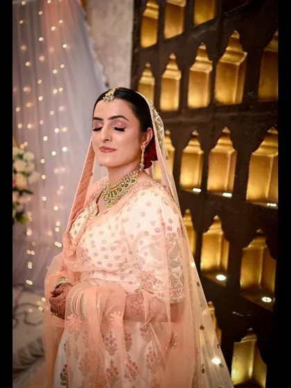 A bride in a lovely peach-colored outfit, her eyes closed in a moment of peace. The warm, golden background lights add a beautiful glow to this serene bridal portrait.