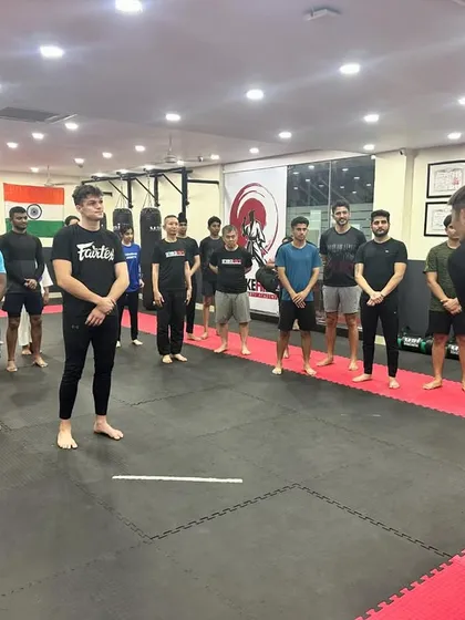 A coach addresses a group of students at the start of a Brazilian Jiu-Jitsu session. Our classes begin with clear instruction, setting the focus for the techniques and drills to come.