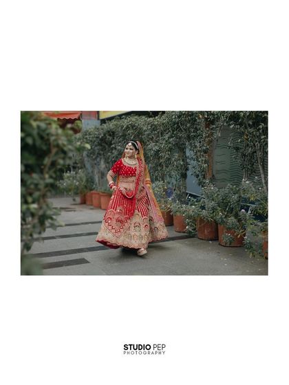 A wide shot of the bride, Payal, twirling in her stunning red and gold lehenga, showcasing its beautiful craftsmanship.