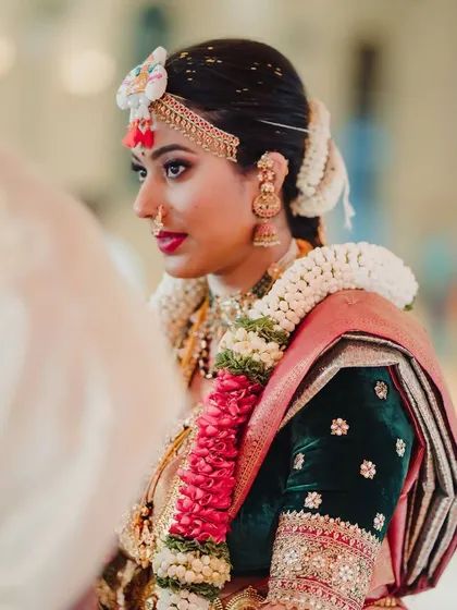 A bride during her wedding ceremony. She wears a dark green velvet blouse with delicate embroidery, providing a rich contrast to her light-colored saree.