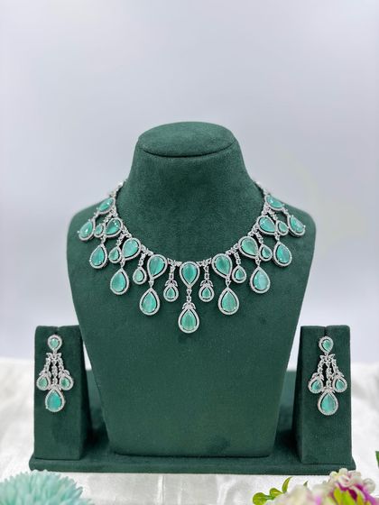 A contemporary silver-plated necklace set with teardrop-shaped stones. This design is available in emerald green, pink, red, and dark blue, offering a sleek and modern look for any occasion.