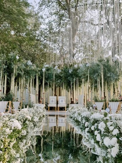 An all-white wedding aisle that is both grand and serene. We lined the mirror walkway with dense white chrysanthemums and hung floral strings from the trees to create this heavenly path.