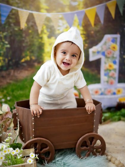 A happy first birthday boy in a rustic, outdoor-themed setup. The wooden cart and "1" sign create a charming scene for his celebration.