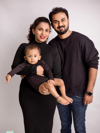 A simple and elegant family portrait. The coordinated black outfits against a light grey background create a sophisticated and modern look.
