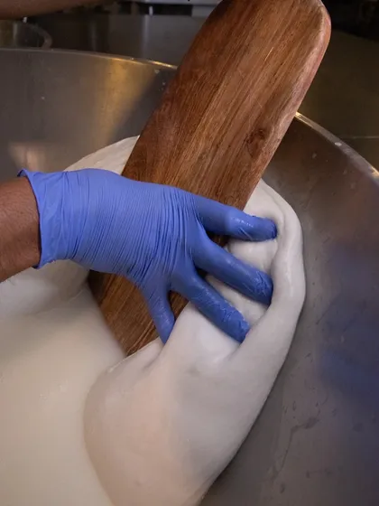 A close-up of the stretching process. The cheesemaker's hands work the curd until it becomes smooth, shiny, and ready to be formed into balls.