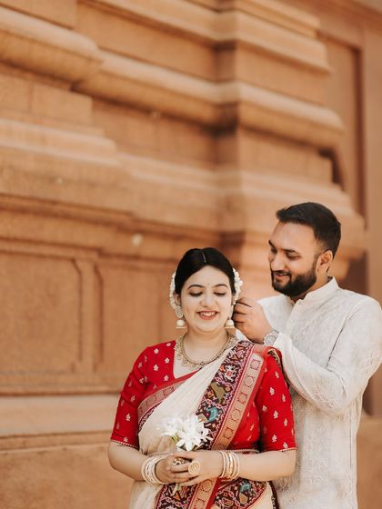 A sweet, detailed shot of the groom helping his bride with her earring. This close-up highlights the intricate details of their outfits and a simple act of care during their heritage photoshoot.