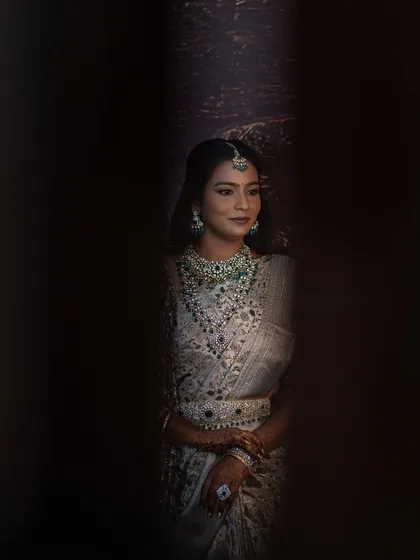 A creative shot of Sruthi, peeking through a gap. The photo creates a sense of mystery and highlights the beauty of her makeup and jewellery.