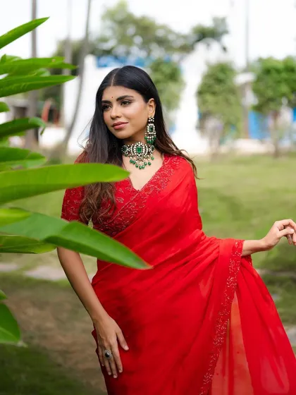 A portrait of a model in a vibrant red saree, framed by green leaves. This composition uses nature to create a beautiful and colorful fashion shot.